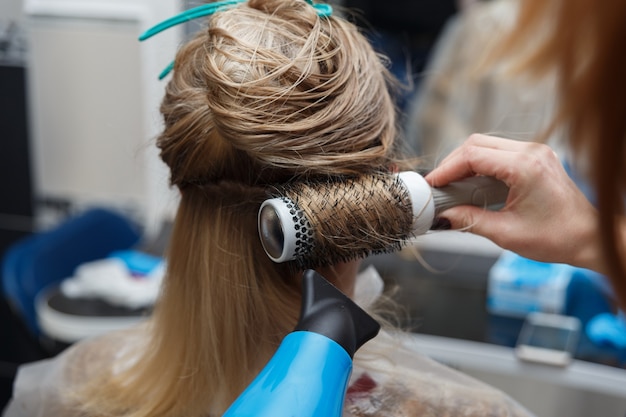 Hairdressers hands drying blond hair with blow dryer and round brush