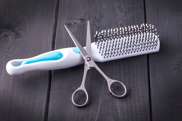 Hairdressing Scissors and massage comb taken from above on a black wooden backdrop