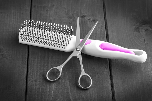 Hairdressing scissors and massage comb taken from above on a black wooden backdrop