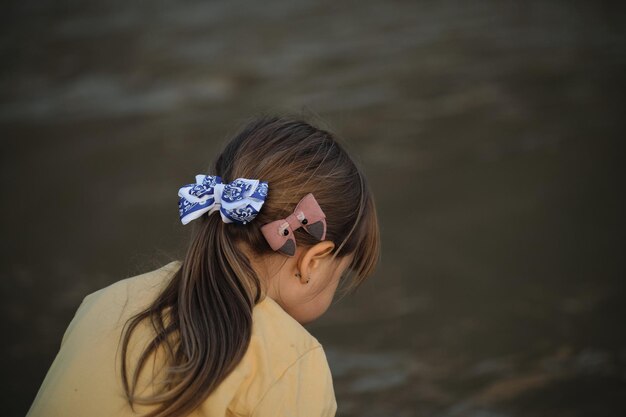 Photo hairstyle of caucasian little girl close up brown hair gathered in tail and two bows blue and pink