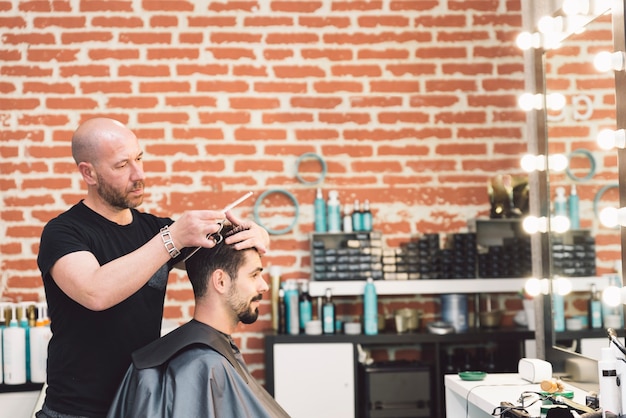 Hairstylist making men's haircut to an attractive man in the beauty salon.