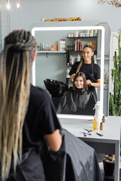 Photo hairstylist spraying hair of happy womanhairdresser with braids