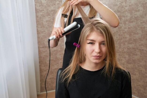 Hairstylist working on woman client with crimper in salon