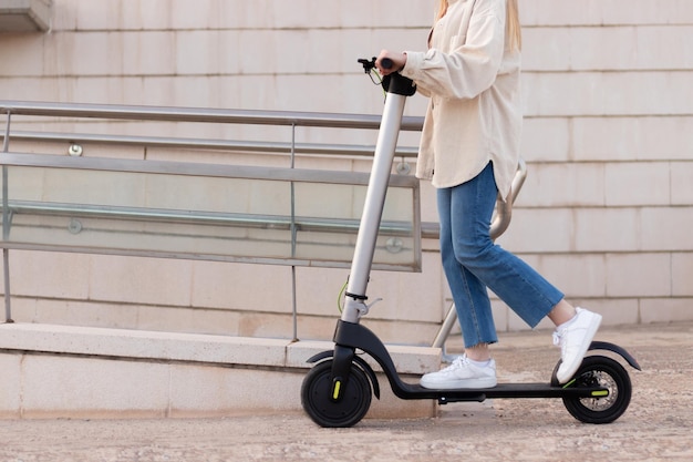 Half cropped view of young unrecognizable woman riding an electric scooter around the city center with buildings around