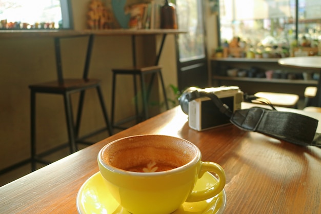 Half cup of cappuccino coffee on a wooden table with a white camera during break time