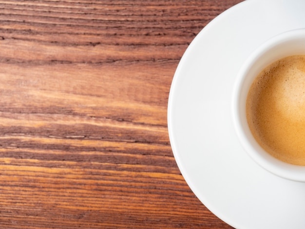 Half a cup of freshly brewed Italian espresso coffee on a wooden background. Delicious foam, white cup and saucer. Copy space, a place for the text. An invigorating drink to wake you up