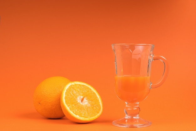 A half-filled glass with a smoothie and a sliced orange on an orange background.