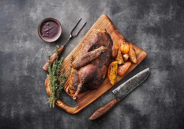 Half goose with sauce and apples baked on a wooden board with a knife and fork against a gray background