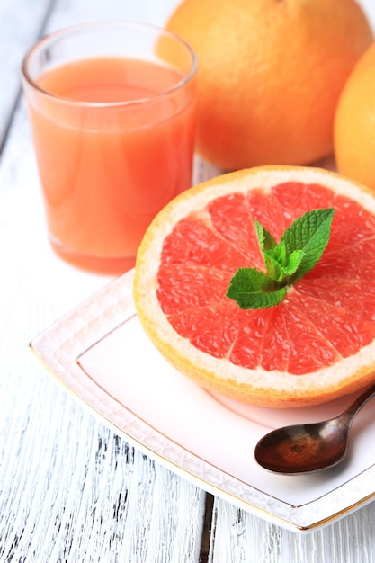 Half of grapefruit glass of fresh juice and spoon on plate on light background