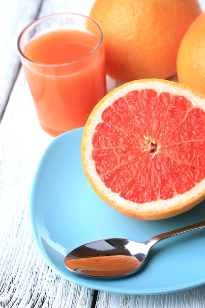 Half of grapefruit glass of fresh juice and spoon on plate on light background