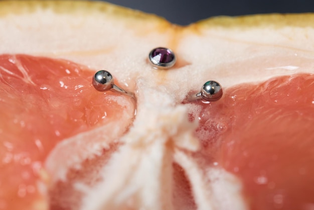 Half of grapefruit with vertical barbell piercing on a background