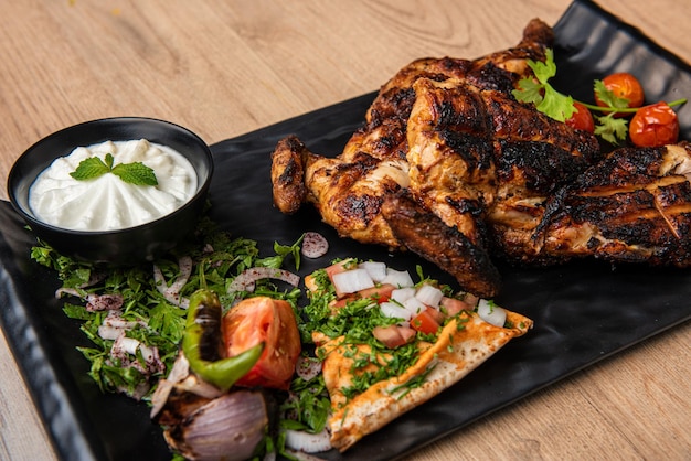 Half grilled chicken with mayo dip and salad served in dish isolated on table top view of arabian food