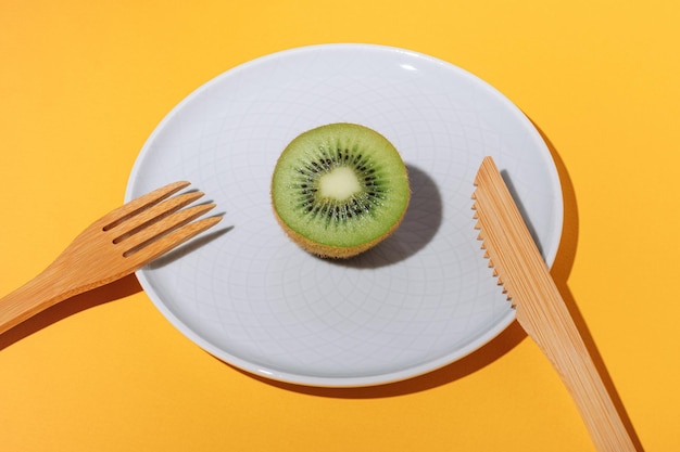 Half of juicy ripe kiwi fruit on a plate and bamboo fork and knife on a yellow background