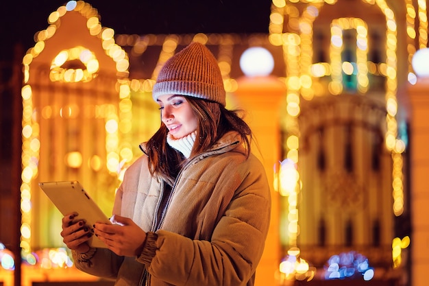 Half length of smiling girl uses her digital tablet while standing outdoor christmas holidays