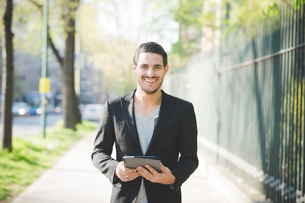 Half length of young handsome italian boy walking through the city using a tablet