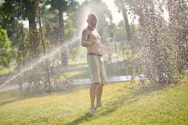 A half-naked man in shorts standing under shower in the park