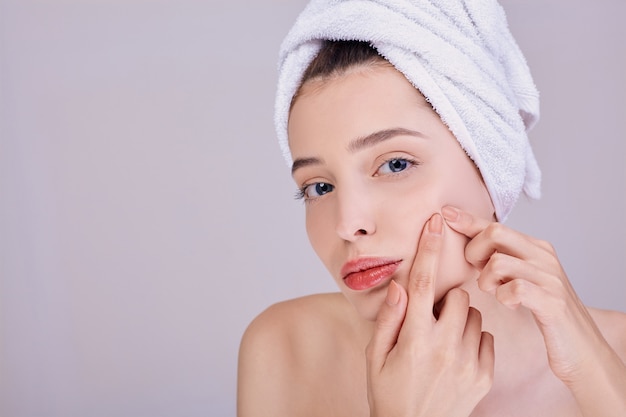 A half-naked woman presses a pimple on her left cheek.