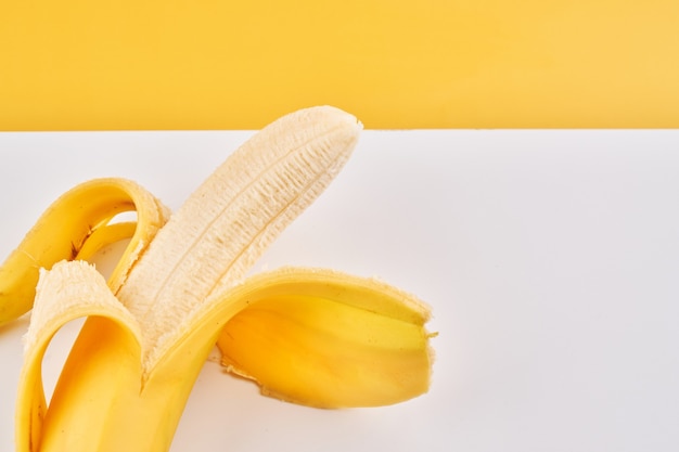 Half peeled banana on yellow white background with copy space