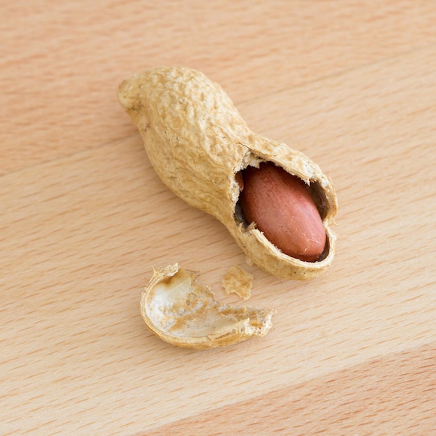 Half peeled peanut with cracked shell on a wooden table