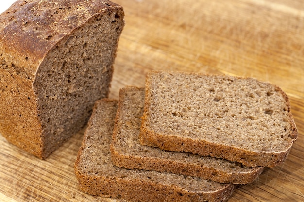 Half of rye brown bread with some bread slices on a chopping board.