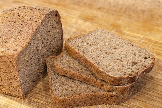 Half of rye brown bread with some bread slices on a chopping board.