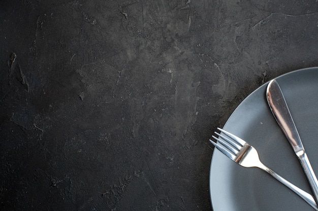 Half shot of cutlery set on a black plate on the left side on dark color background with free space