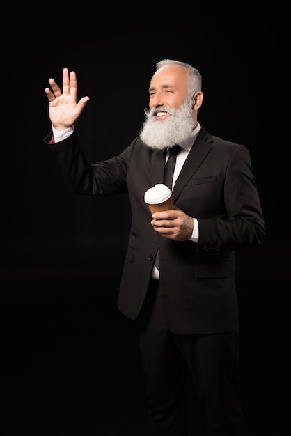 Halflength shot of smiling businessman in a suit with a cup of coffee and waving his hand at