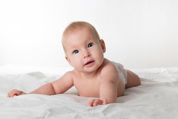 A halfyearold beautiful baby in a diaper lies on his stomach and looks at the camera with different emotions