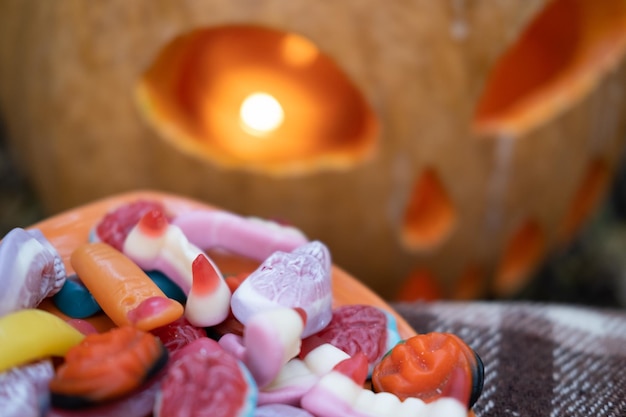 Halloween background. scary candies on a plate near pumpkin with candle