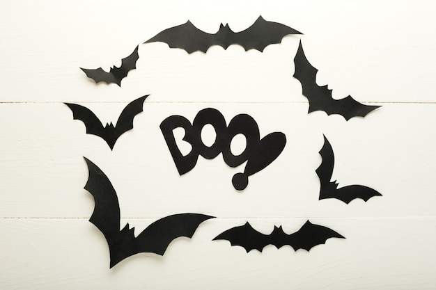 Halloween background with paper bats and BOO lettering on white wooden background. Halloween holiday decorations. Flat lay, top view, copy space. Party invitation mockup, celebration.