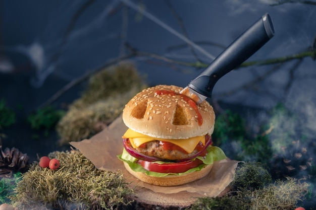 Halloween burger in a shape of pumpkin head jack lantern in a mystery forest. Scary cheeseburger