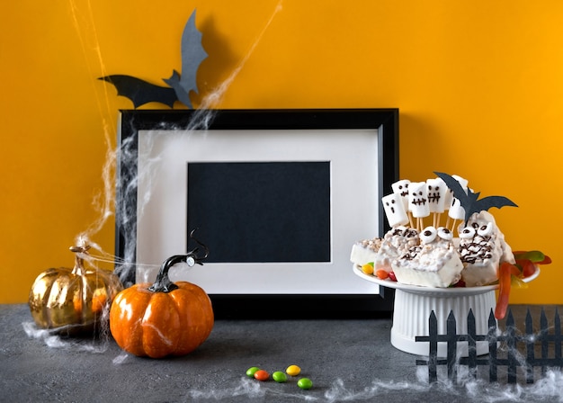 Halloween candy bar: funny monsters made of biscuits with chocolate and gummy worms, ghosts marshmelow close-up on the table