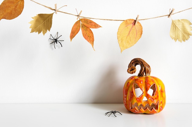 Halloween composition with ceramic pumpkin jack lantern and floral garland on table wall background Home decoration