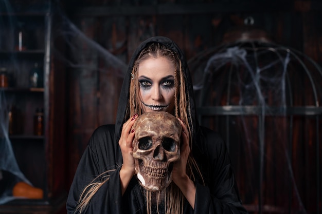 Halloween concept Witch portrait close up with dreadlocks looking camera dressed black hood standing dark room with cage on background