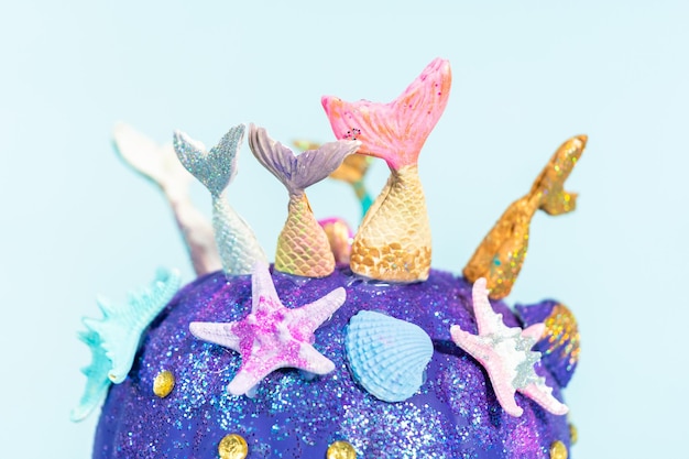 Halloween craft pumpkins decorated with mermaid tails, glitter, and sparkly rhinestones on a blue background.