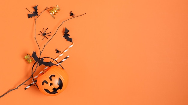 Halloween decorations paper bats flying on tree branch and pumpkin bucket on orange background