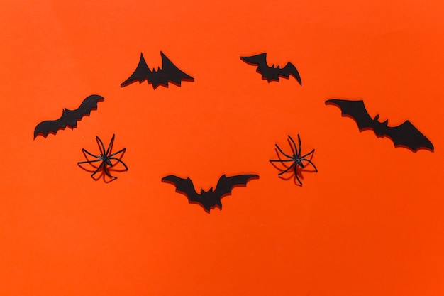 Halloween, decorations and scary concept. Spiders and black bats fly over bright orange