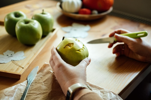 Halloween diy fruit ideas female hands cutting out halloween green apple with creepy carved face on