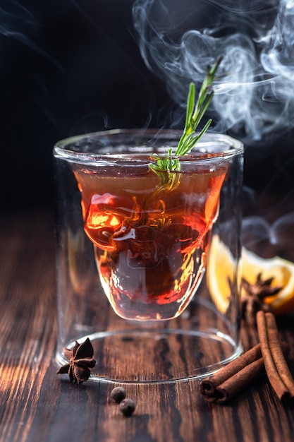 Halloween drinks. Whiskey, rum, or bourbon poured into a transparent skull-shaped glass. Mystical setting and smoke around. Close-up.