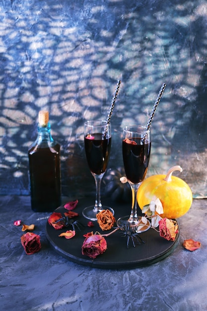 Halloween drinks wine pumpkins mystical decorations dry roses and shadows on a black background