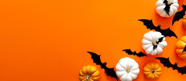 Halloween flat lay composition of black paper bats fand pumpkins on orange background Halloween concept