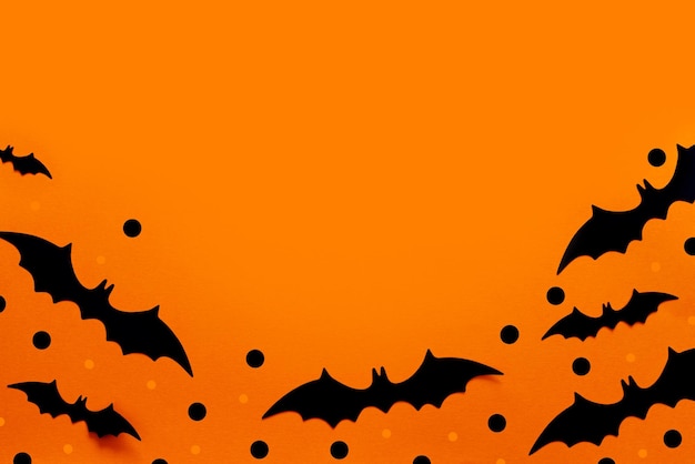 Halloween flat lay composition of black paper bats fand pumpkins on orange background Halloween concept