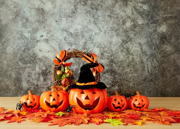 Halloween holiday decoration with pumpkin head jack lantern and autumn leaves on table wood with concrete wall background, halloween background concept, copy space.