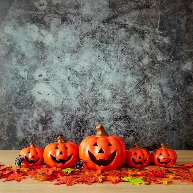 Halloween holiday decoration with pumpkin head jack lantern and autumn leaves on table wood with concrete wall background, halloween background concept, copy space.