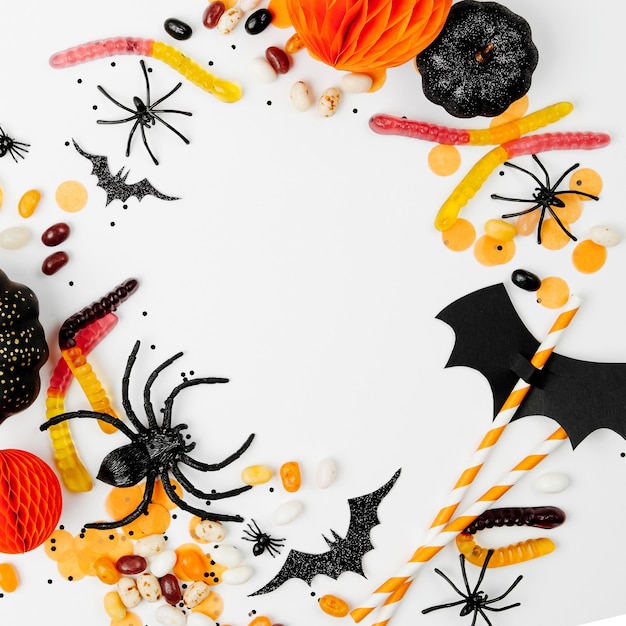 Halloween holiday frame with colorful candy, bats, spiders, pumpkins and decorations on white background. Flat lay. View from above