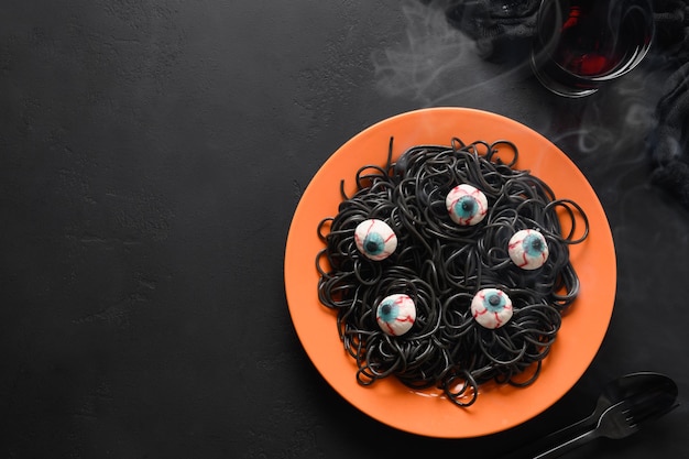 Halloween Italian black pasta decorated horror eyes in orange plate on black