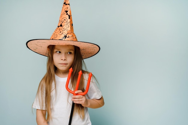 Halloween kids girl fooling around with little devil trident on blue background with copy space Ready for the weekend with jokes or treats