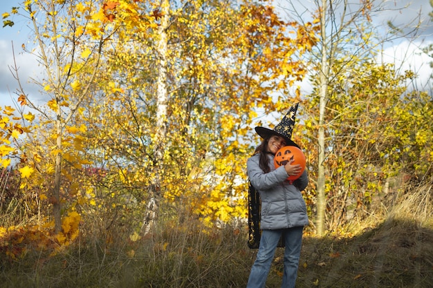 Halloween kids. Little girl with jack o' lantern in witch hat with pumpkin. Toddler kid in witch costume playing in autumn park. A Child in a carnival costume outdoors