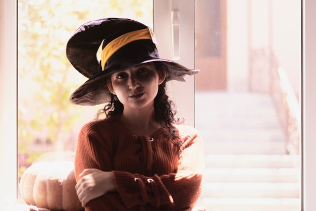 Halloween lady wearing witch cup a woman in witch hat and halloween pumpkin near the windows portrai...