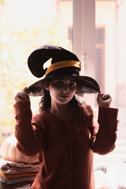 Halloween lady wearing witch cup a woman in witch hat and halloween pumpkin near the windows portrai...